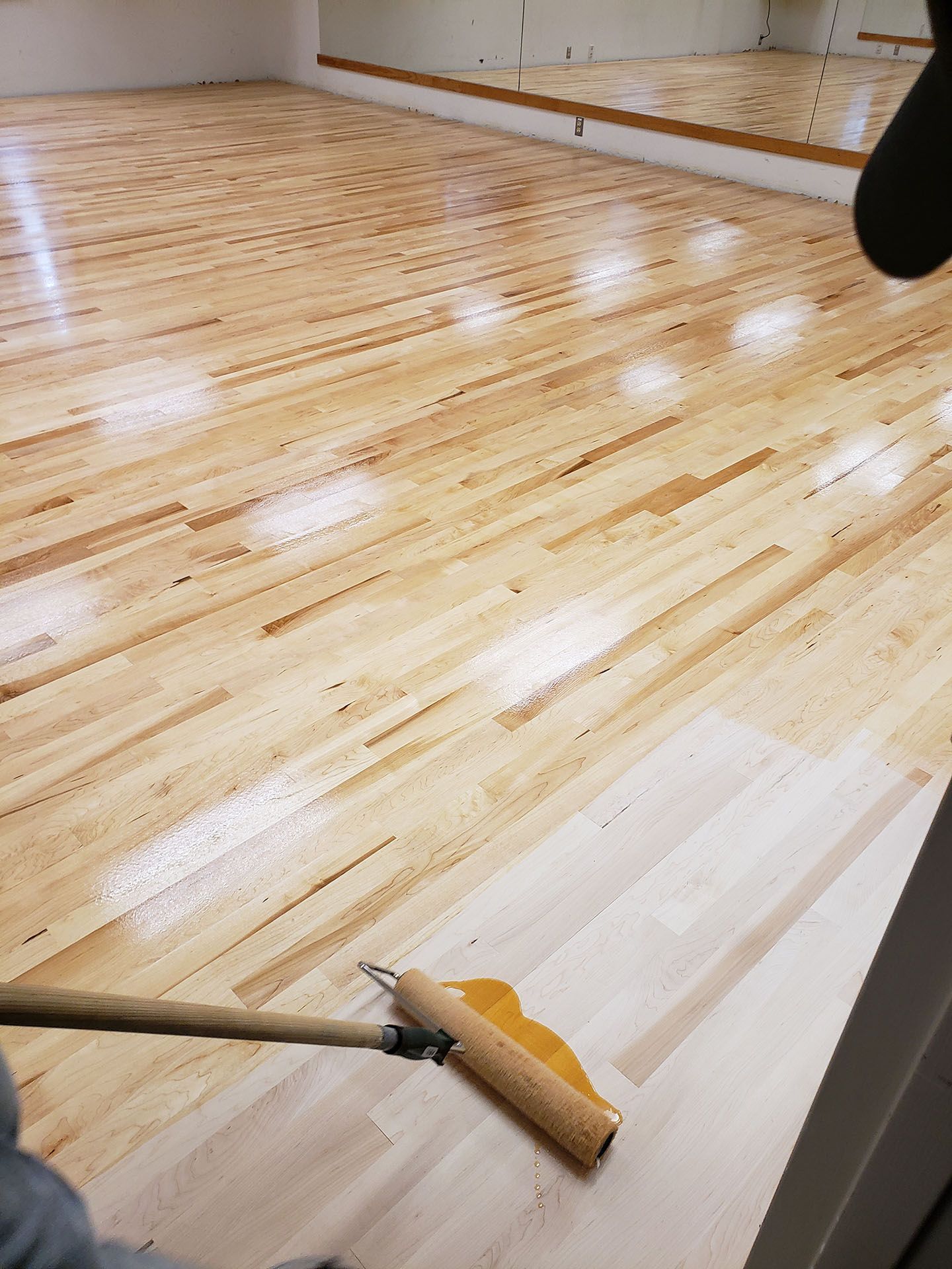 A person is painting a wooden floor with a roller
