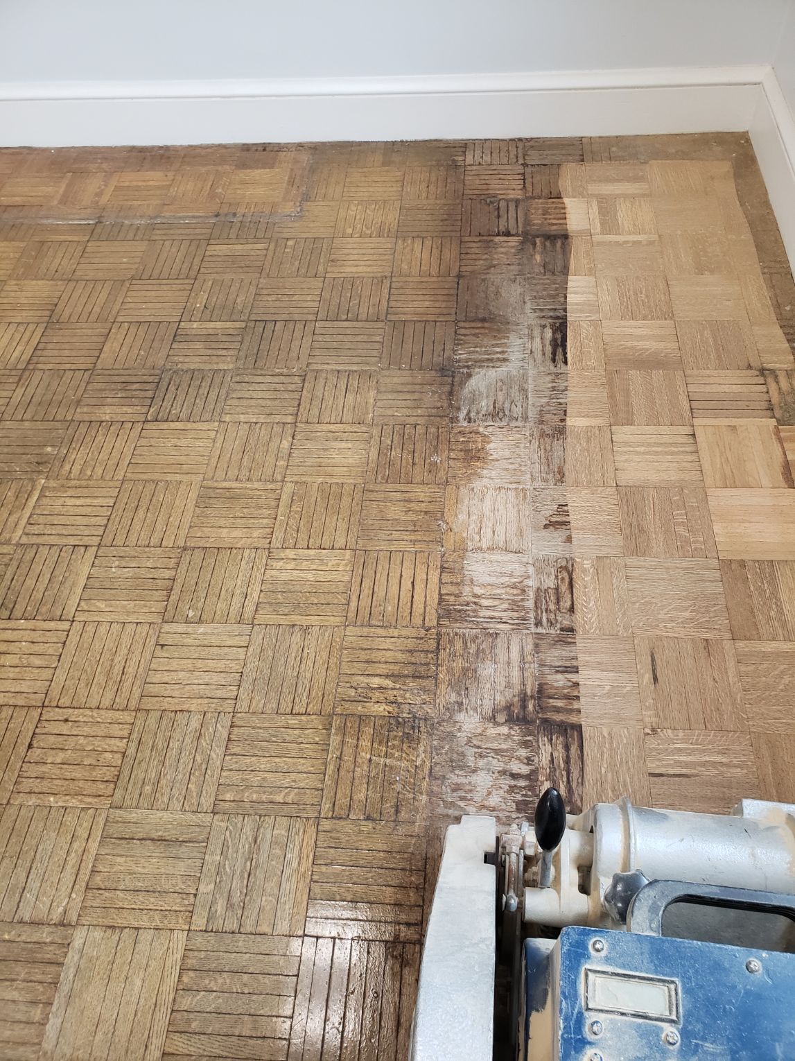 A wooden floor is being sanded with a machine