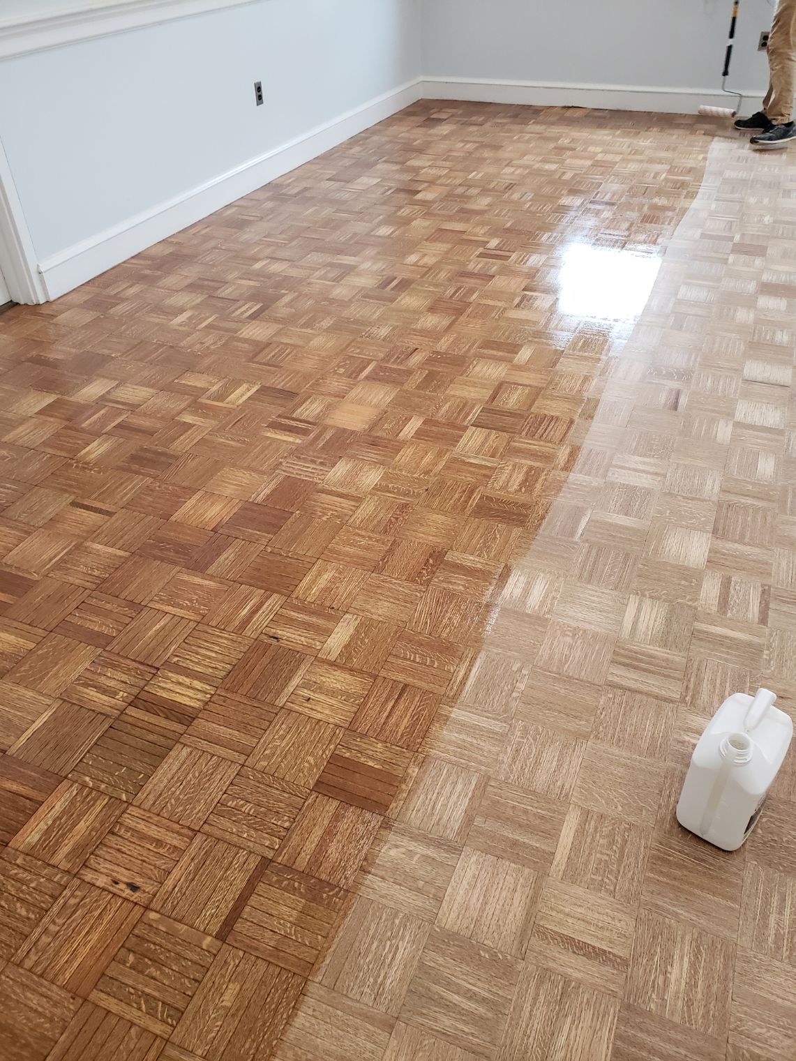 A person is painting a wooden floor in a living room