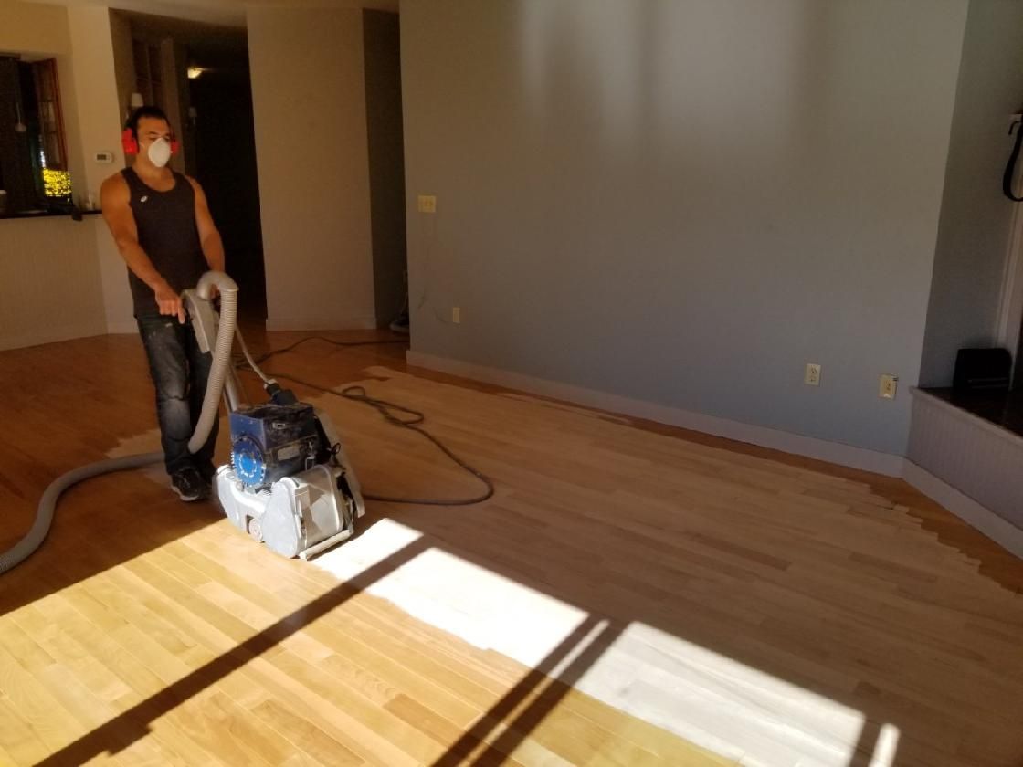 A man wearing a mask is using a vacuum cleaner on a wooden floor