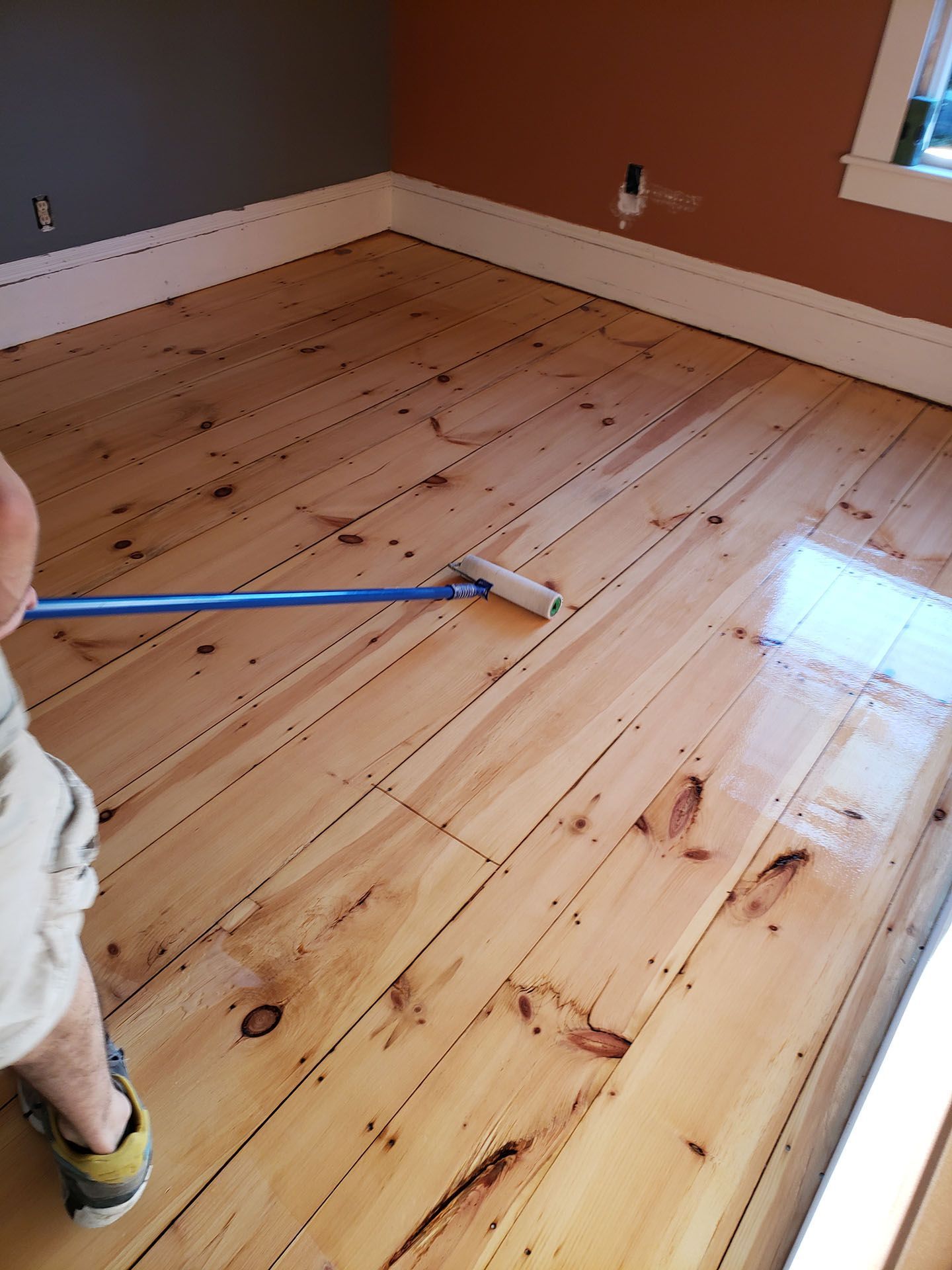 A child is painting a wooden floor with a roller