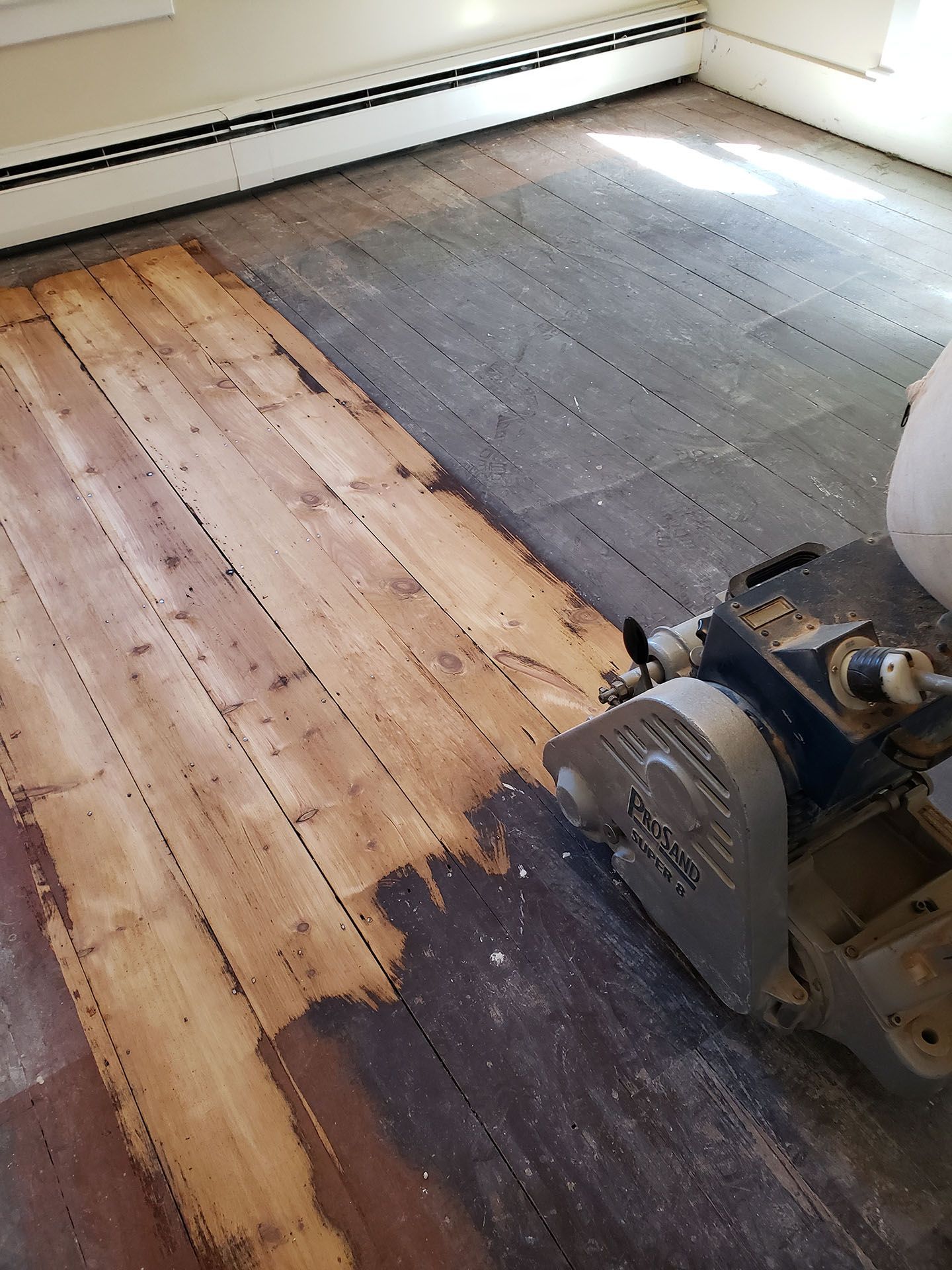 A person is sanding a wooden floor with a machine