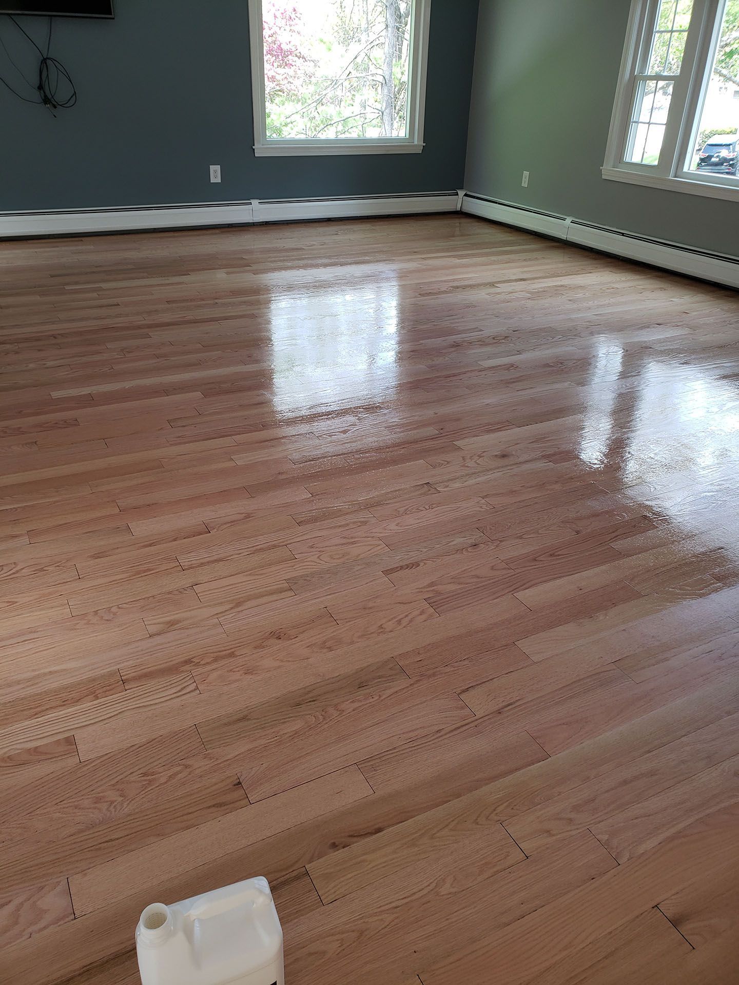 A large wooden floor in a living room with a bottle of polish on it