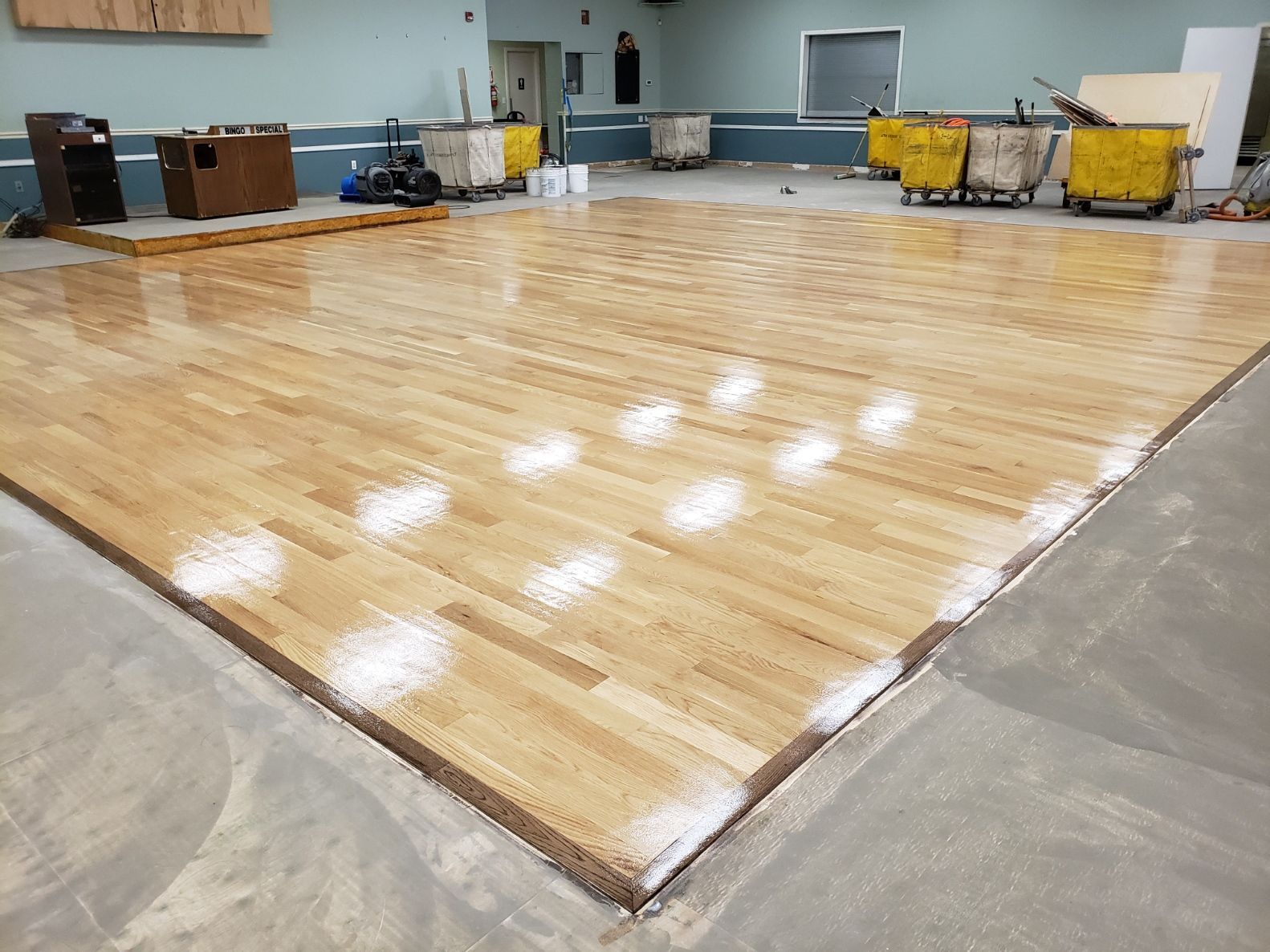 A large wooden floor is being painted white in a room