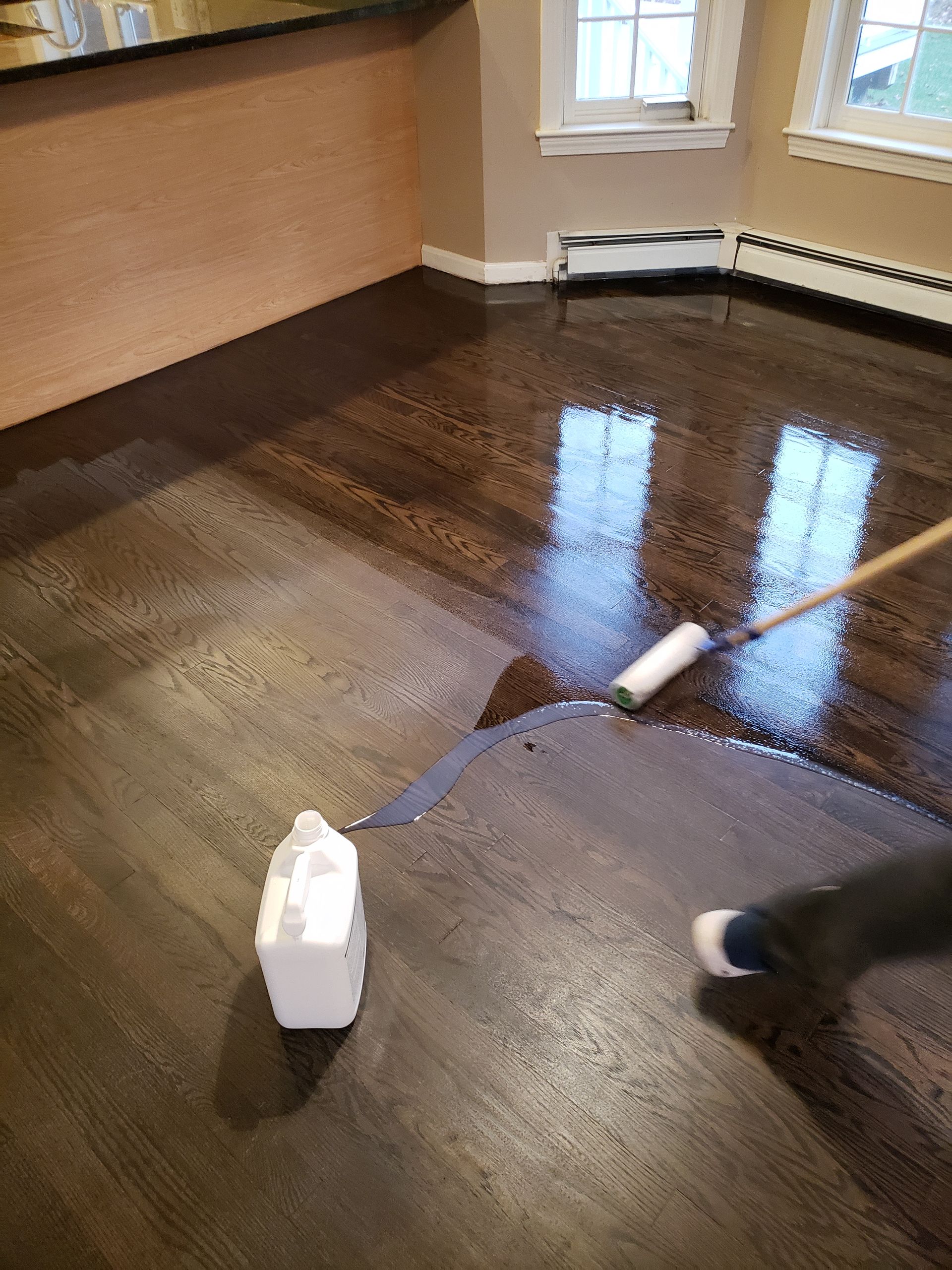 A person is painting a wooden floor with a roller