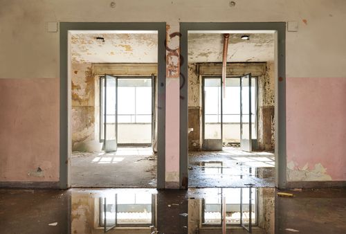 Abandoned building interior with two open doorways, peeling pink walls, and reflections on a wet floor