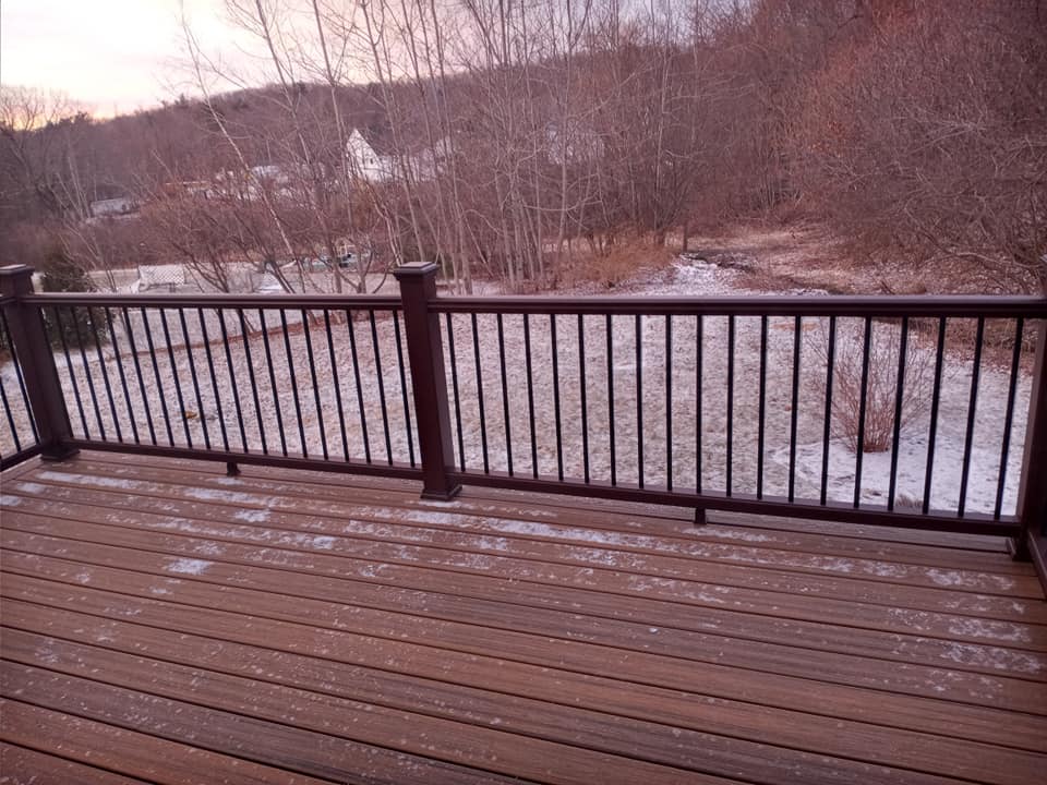 A wooden deck with a metal railing overlooking a snowy field.