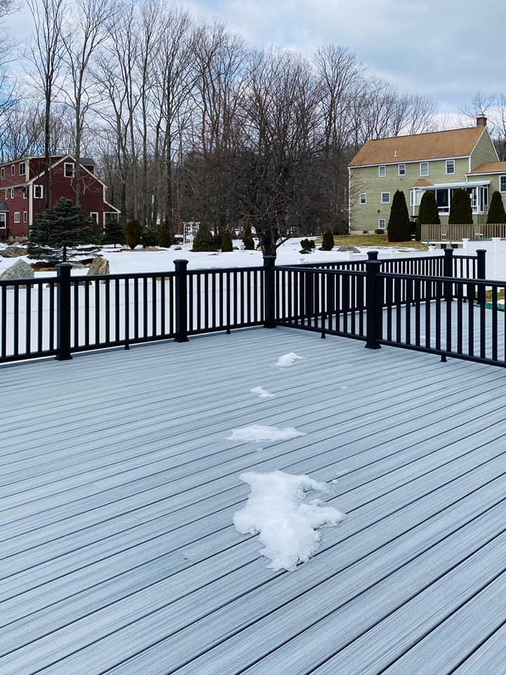 A snowy deck with a black railing and a house in the background