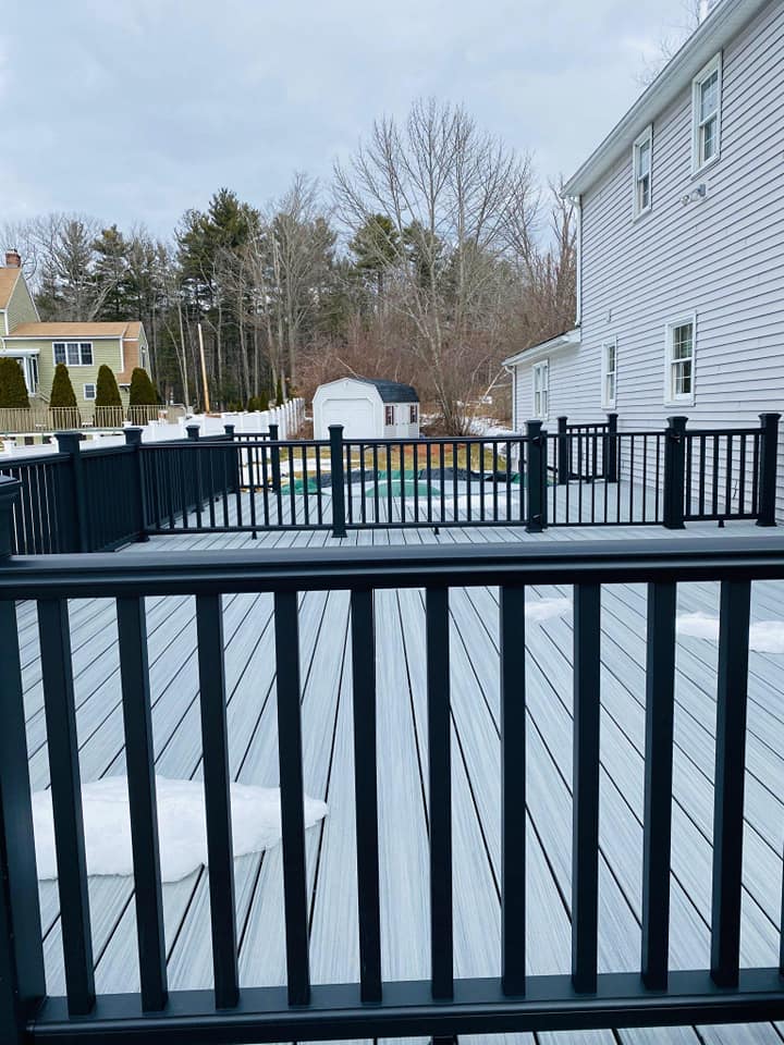 A deck with a black railing and a house in the background.
