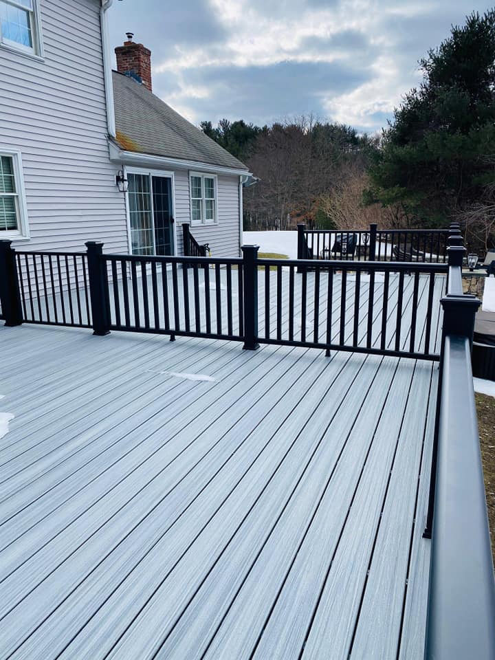 A deck with a black railing and a white house in the background.