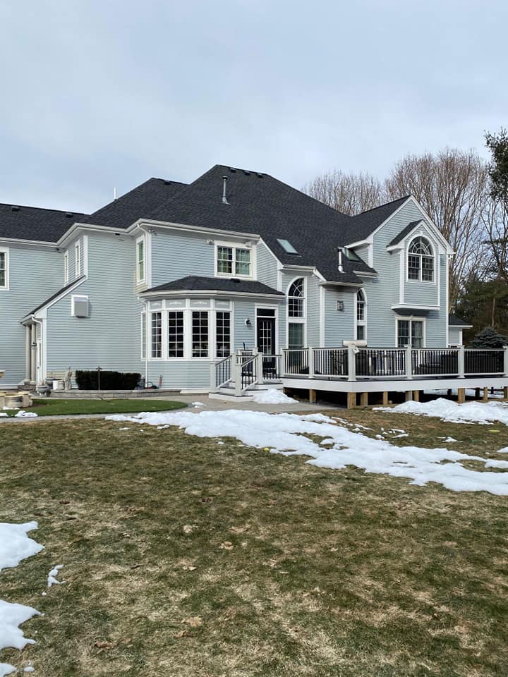 A large white house with a black roof is sitting on top of a lush green field.