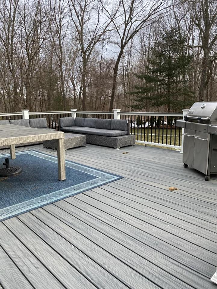 A wooden deck with a couch , table , and grill.