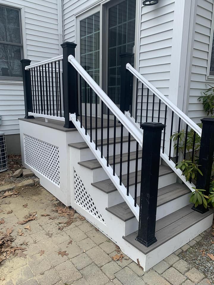 A white house with a black railing and stairs leading up to it.