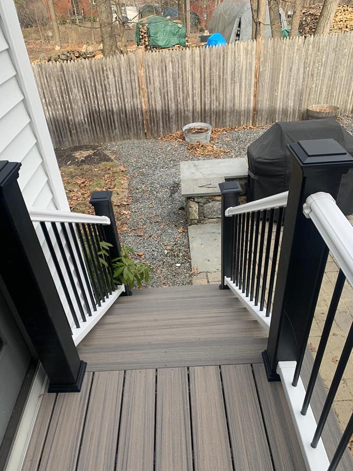 A deck with stairs leading up to a fence and a grill.