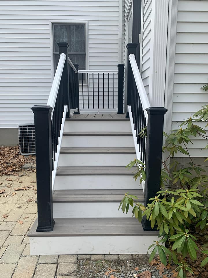 A set of stairs leading up to a white house with a black railing.