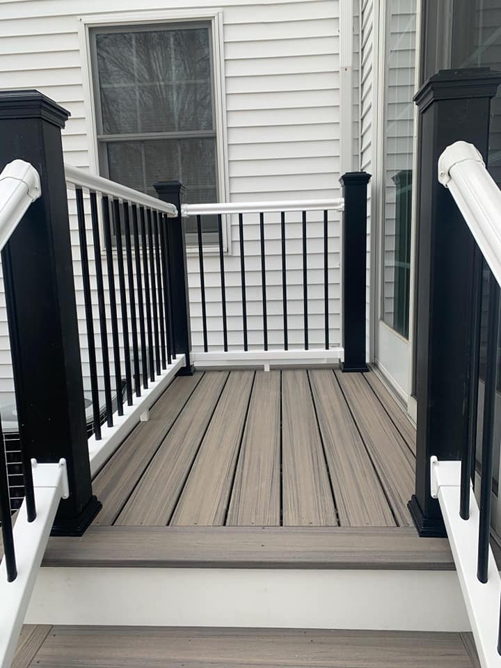 A wooden deck with a black railing and stairs leading to it.