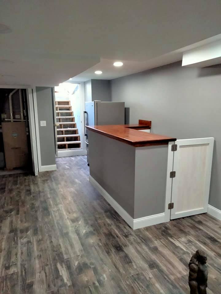 A basement with hardwood floors , a counter and stairs.