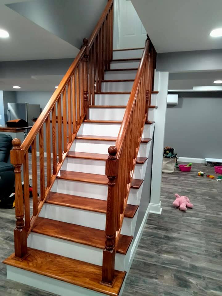 A wooden staircase with white steps and a wooden railing in a basement.