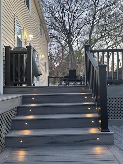 A deck with stairs leading up to it and a house in the background.