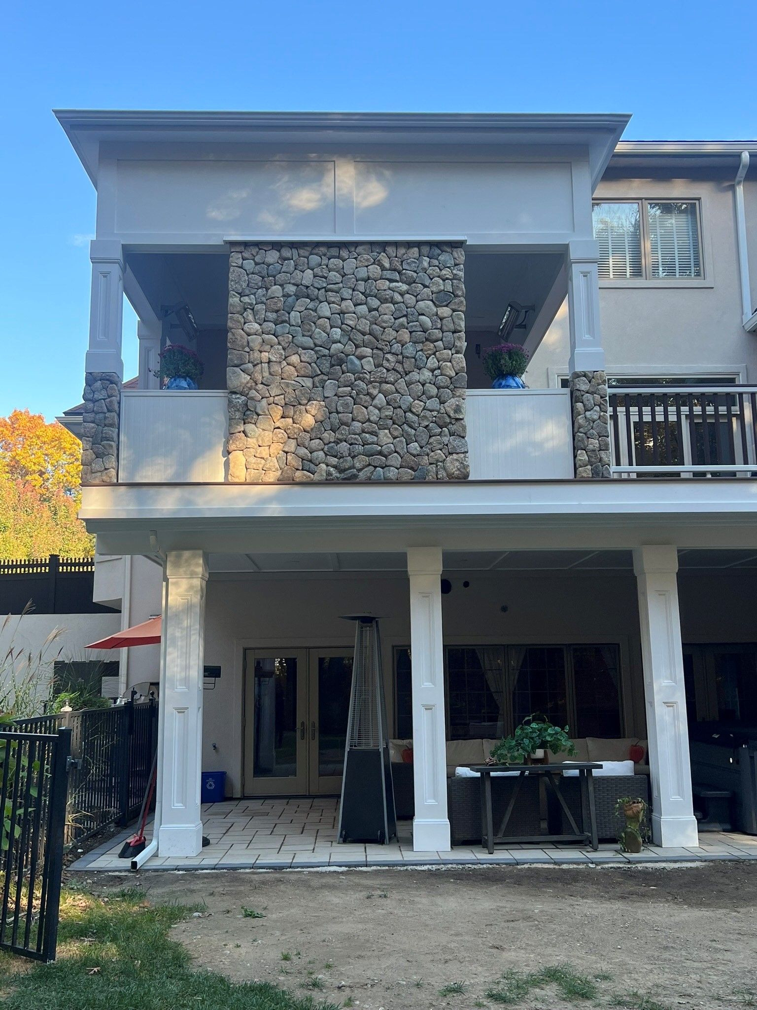 The back of a house with a stone wall and a large porch.
