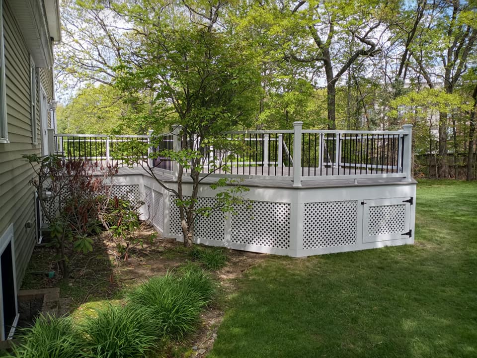 A white deck with a black railing is in the backyard of a house.