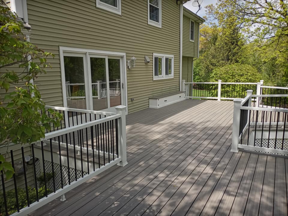 A large deck with a white railing is in front of a house.