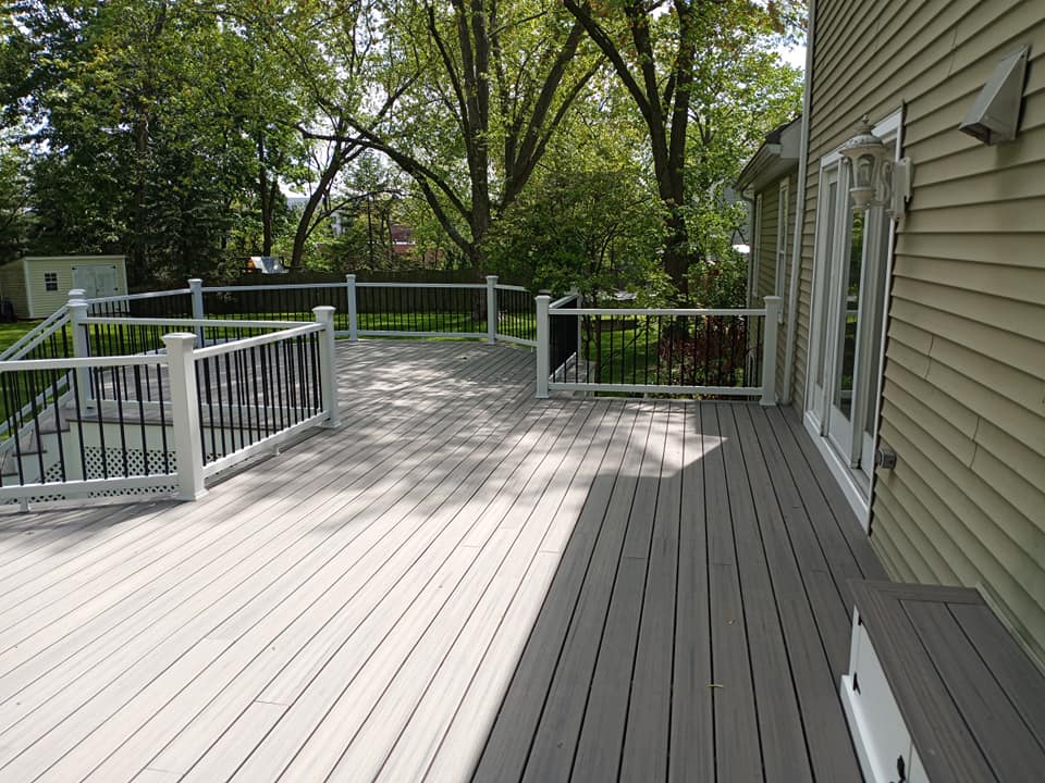 A large wooden deck with a white railing and stairs is sitting in front of a house.