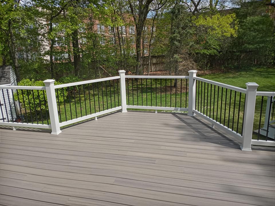 A wooden deck with a white railing and trees in the background.
