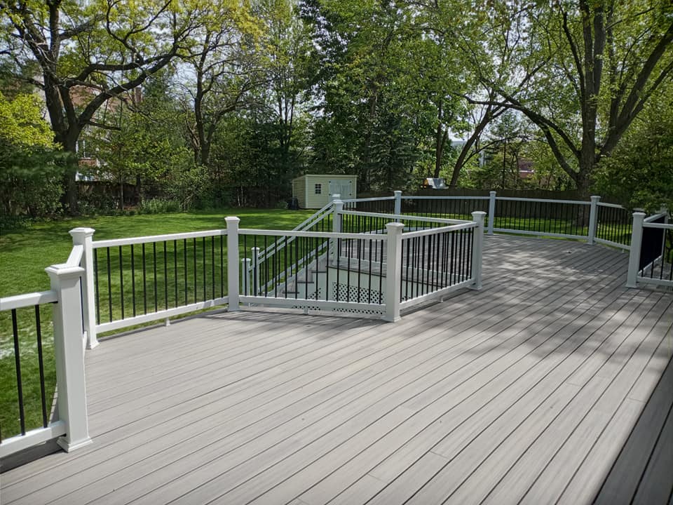 A large gray deck with a white railing and stairs leading up to it.