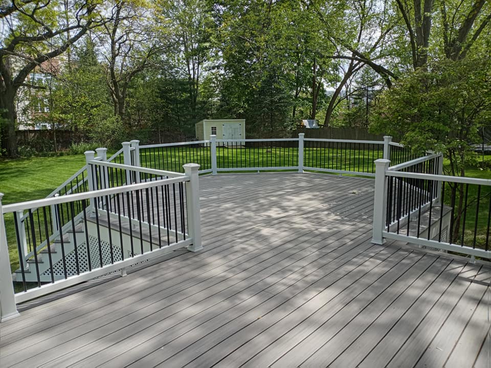 A large wooden deck with a white railing and stairs surrounded by trees.