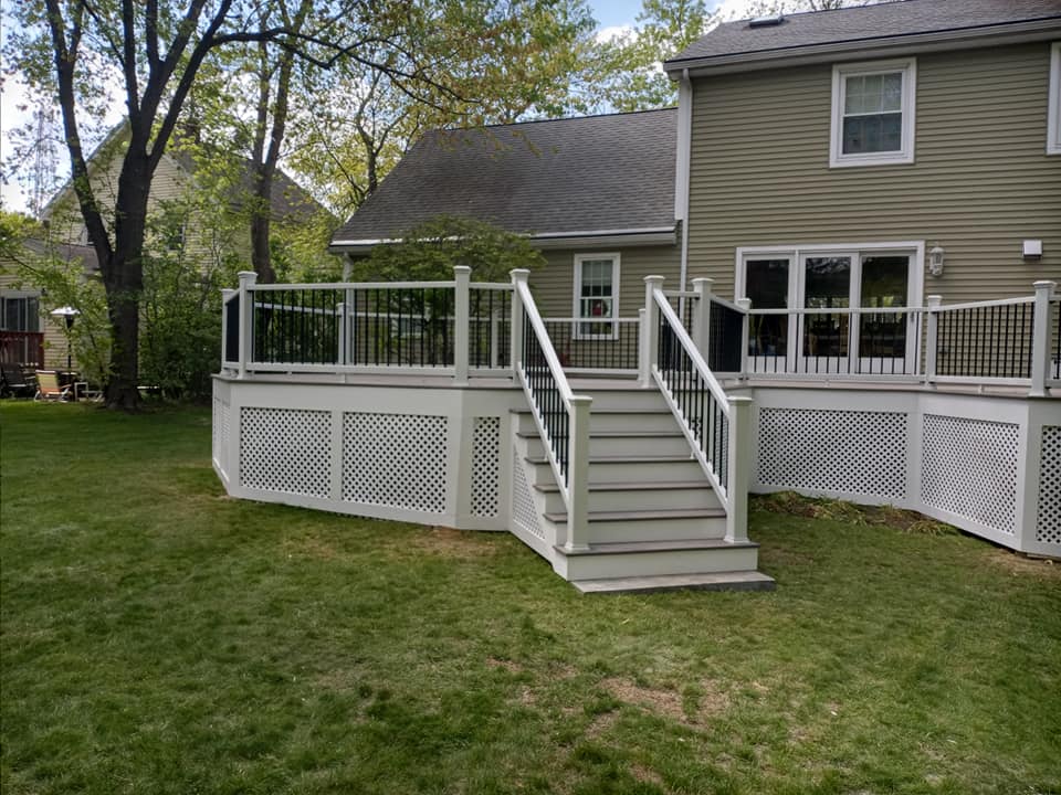 A large deck with stairs leading up to it is in the backyard of a house.
