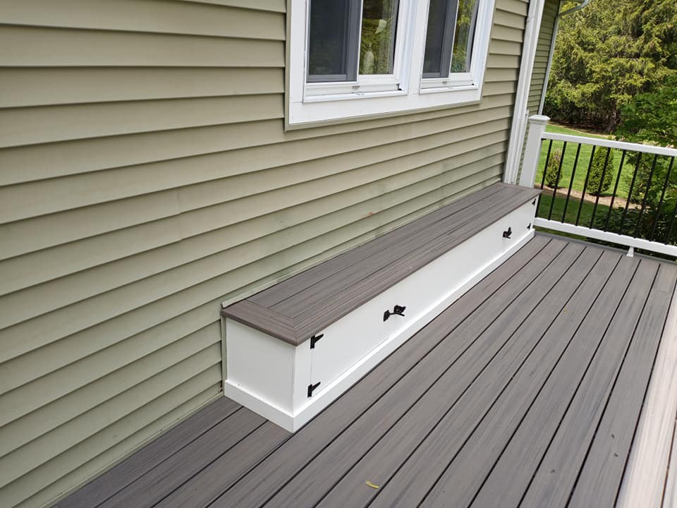 A bench on a deck next to a house with a window.