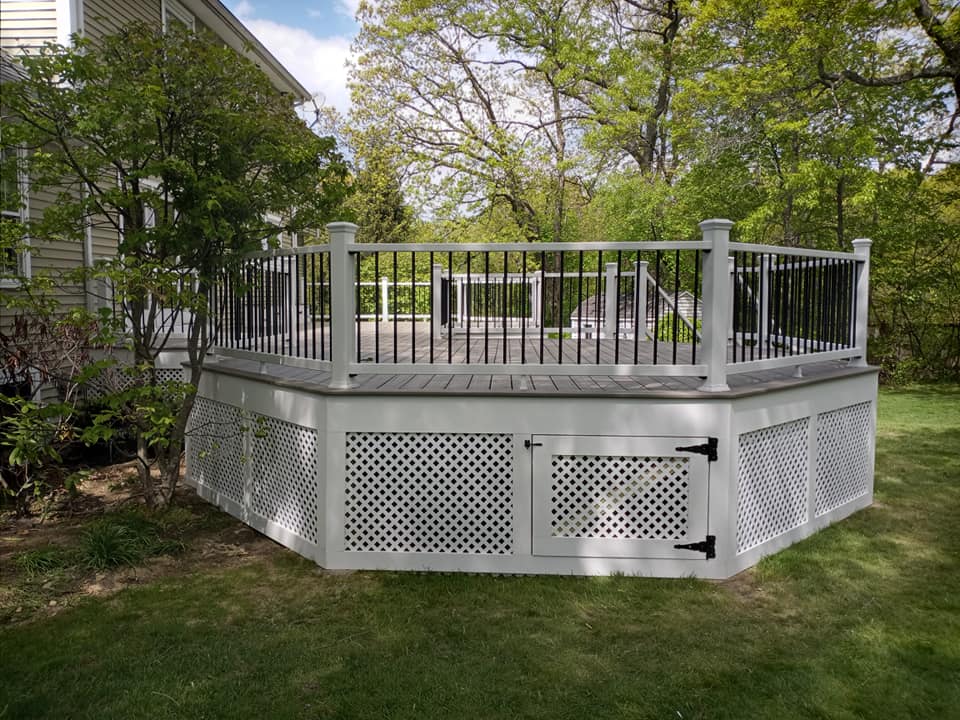 A white deck with a black railing is in the backyard of a house.