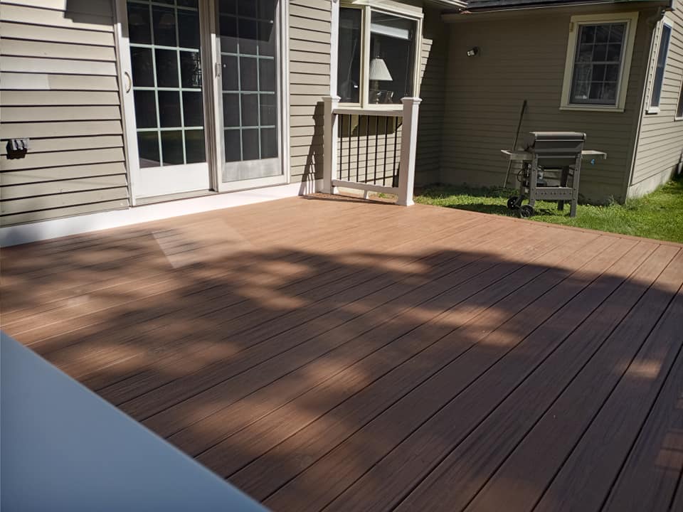 A wooden deck with a grill on it in front of a house