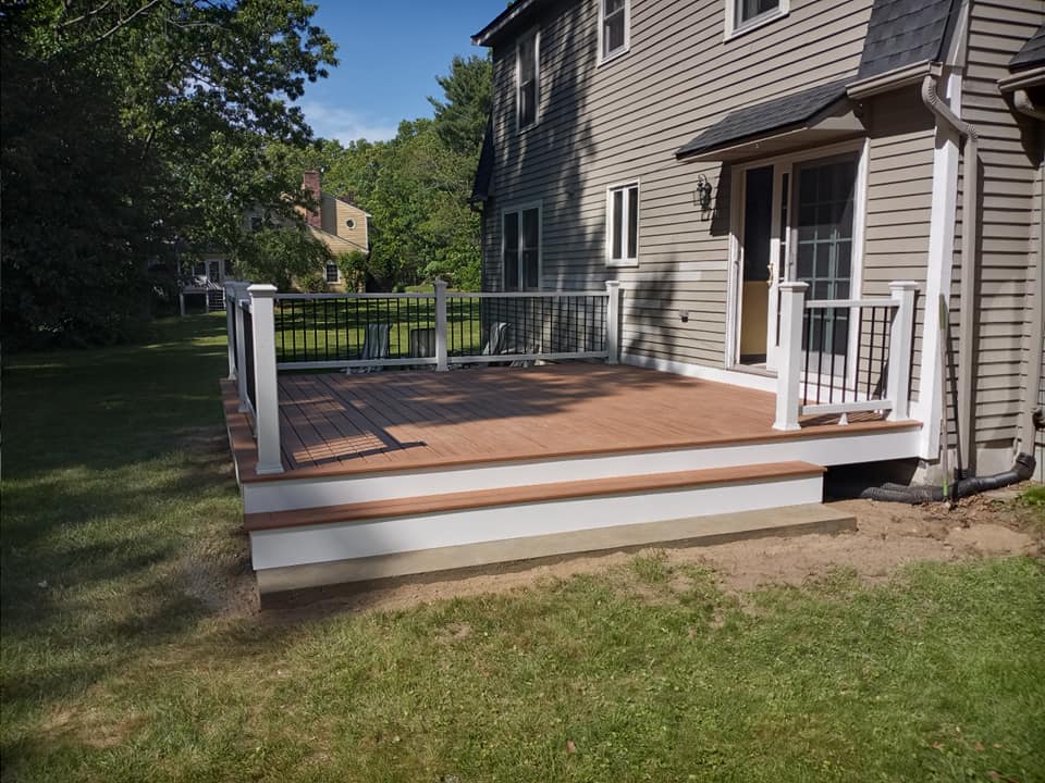 A large deck with a white railing is in the backyard of a house.