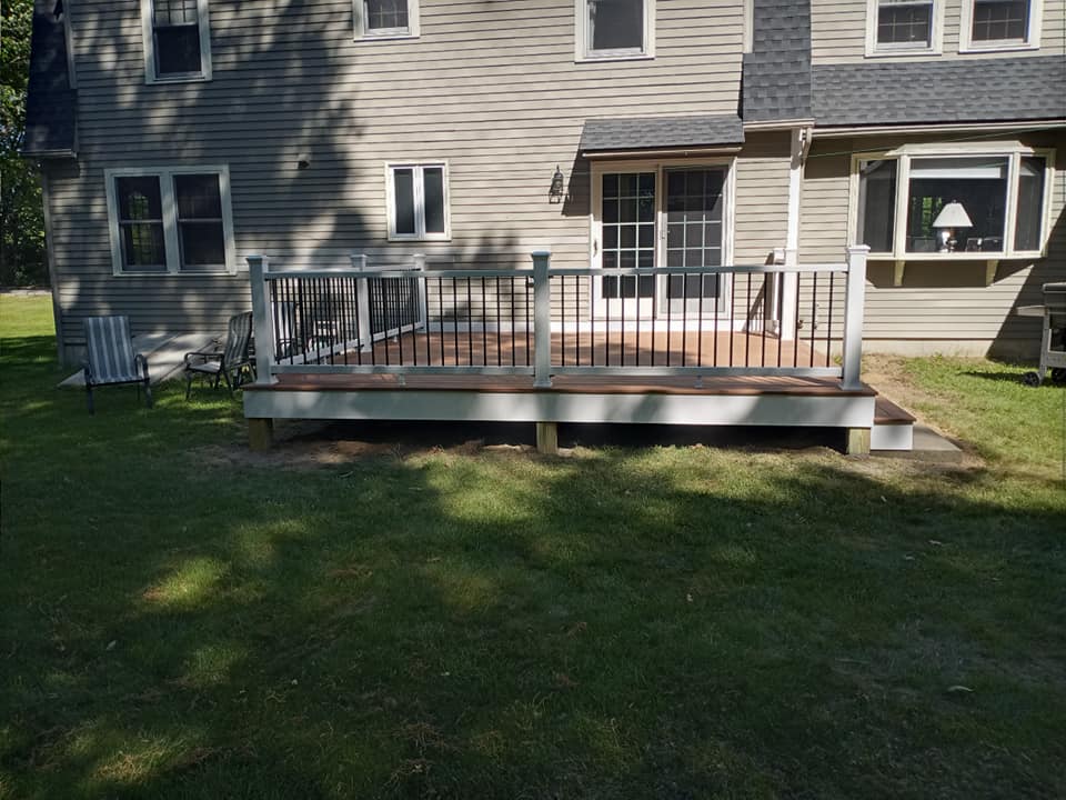 A deck with a railing is in the backyard of a house.