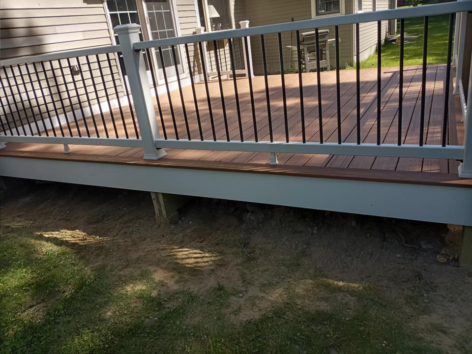 A wooden deck with a metal railing and a house in the background