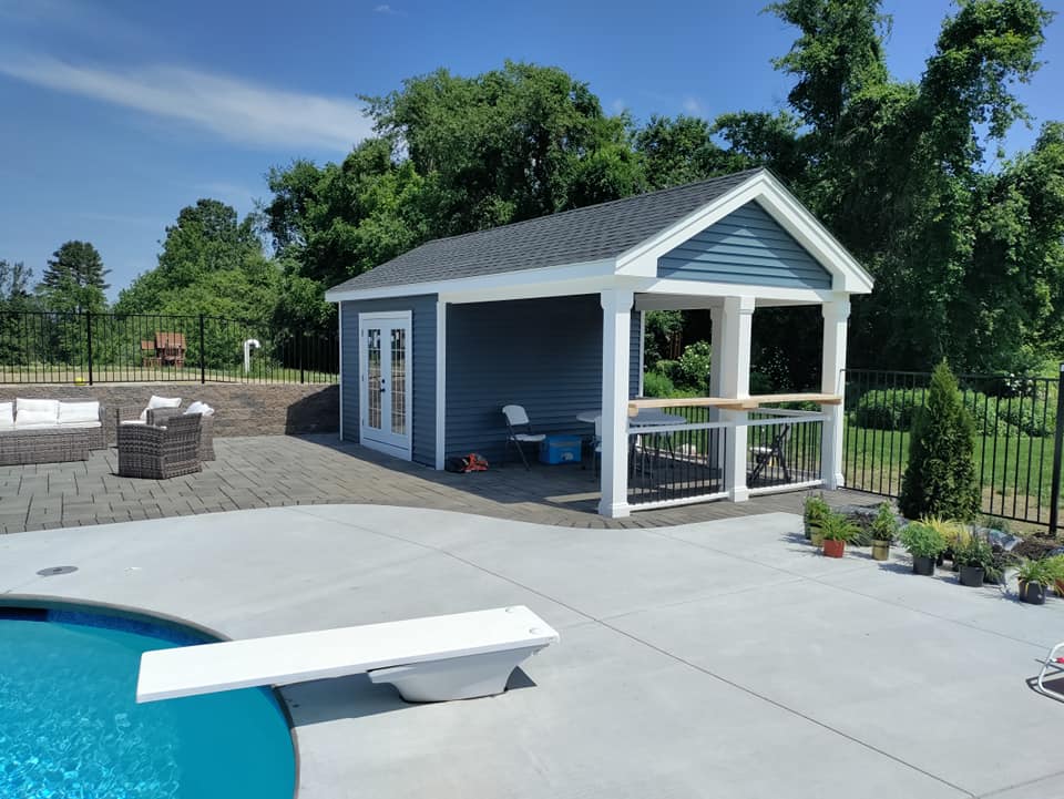 A shed with a porch and a diving board next to a pool.