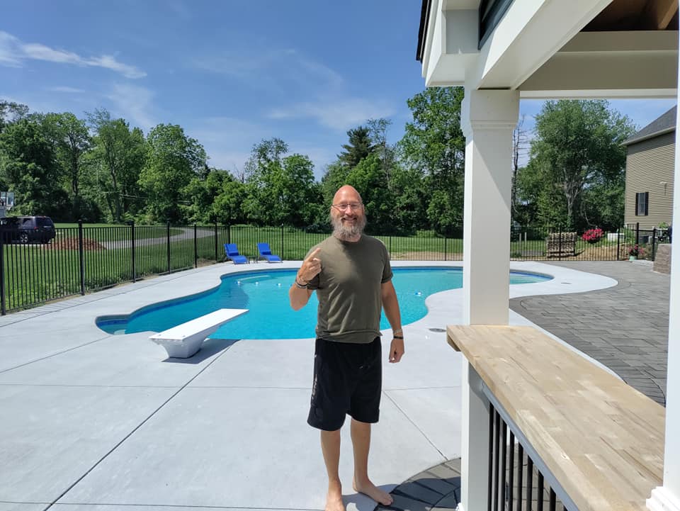 A man is standing in front of a swimming pool giving a thumbs up.