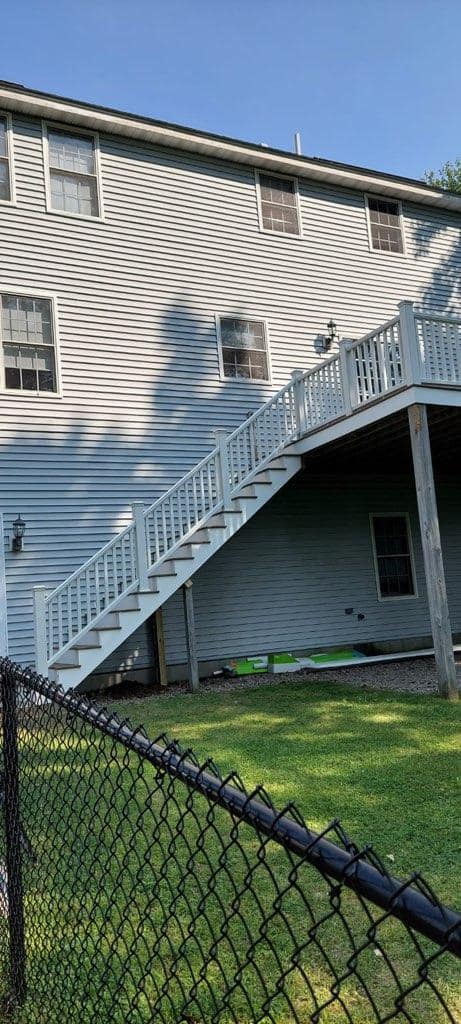 A house with stairs leading up to a deck behind a chain link fence.