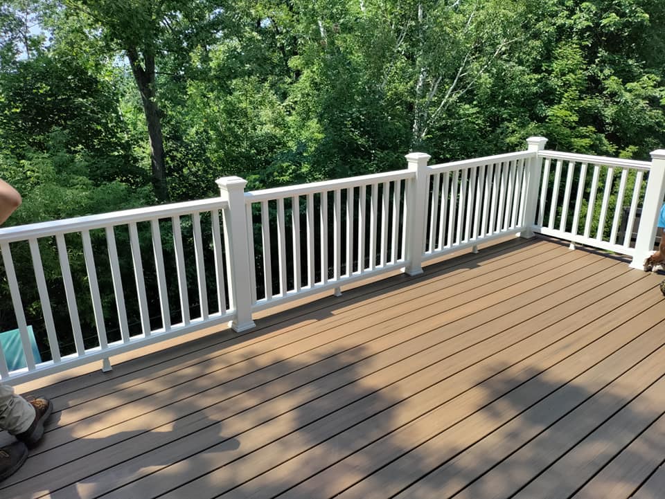 A wooden deck with a white railing and trees in the background.