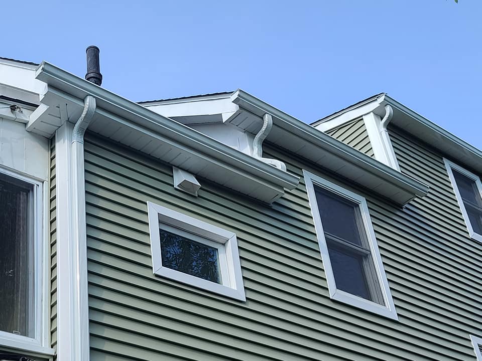 A house with green siding and white windows has a chimney on the roof