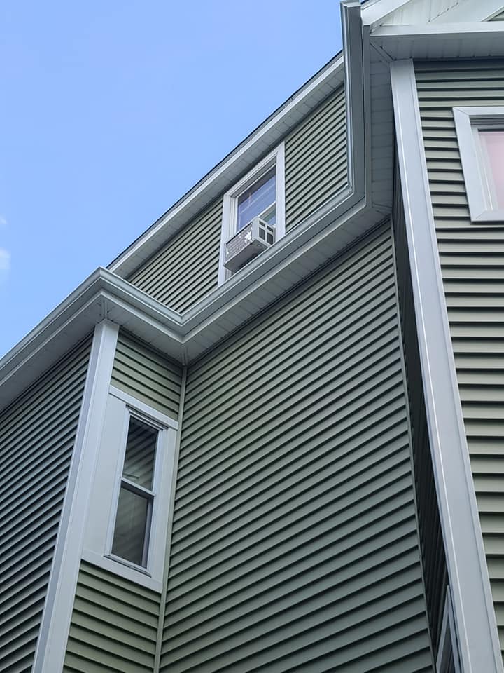 A house with green siding and white windows is against a blue sky.