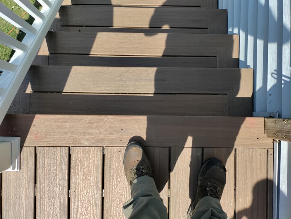 A person 's feet are standing on a wooden deck.