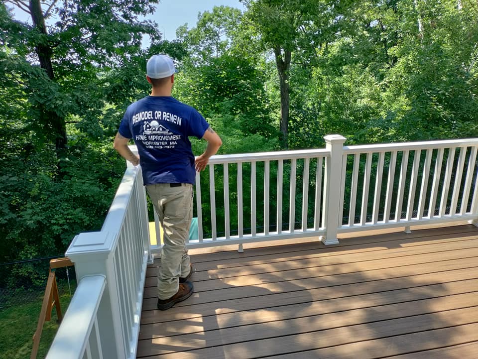 A man is standing on a deck looking out over a forest.