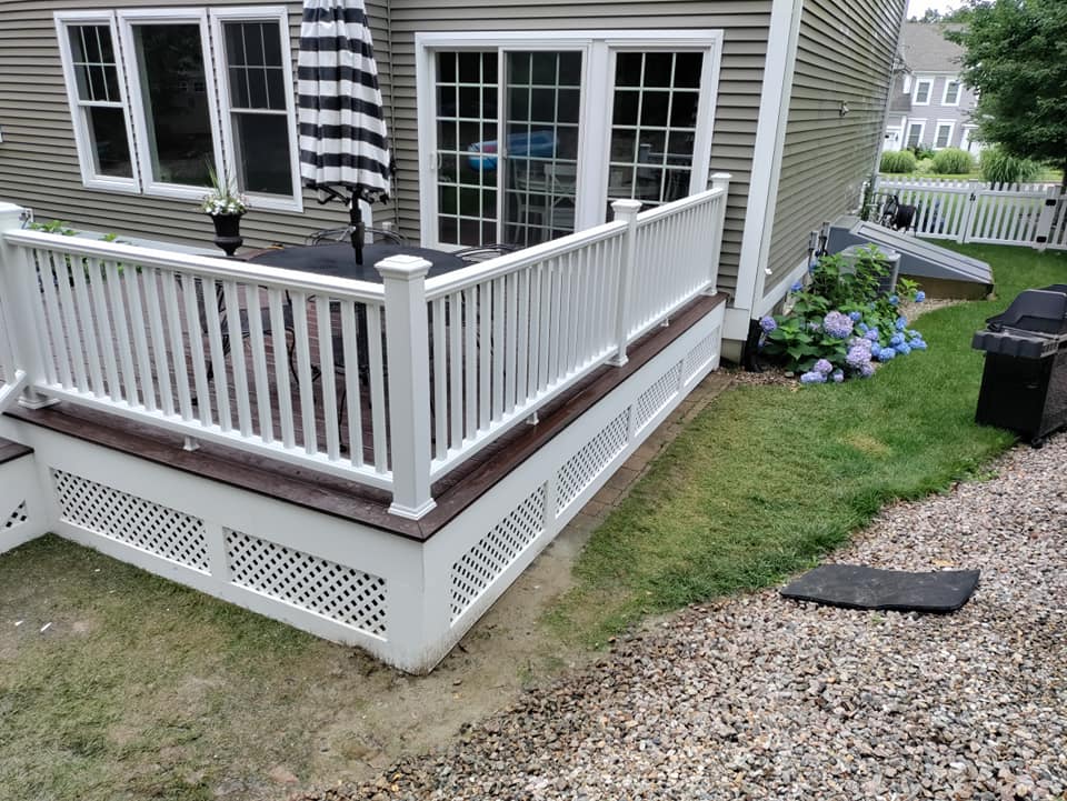 A deck with a table and umbrella on it in front of a house.