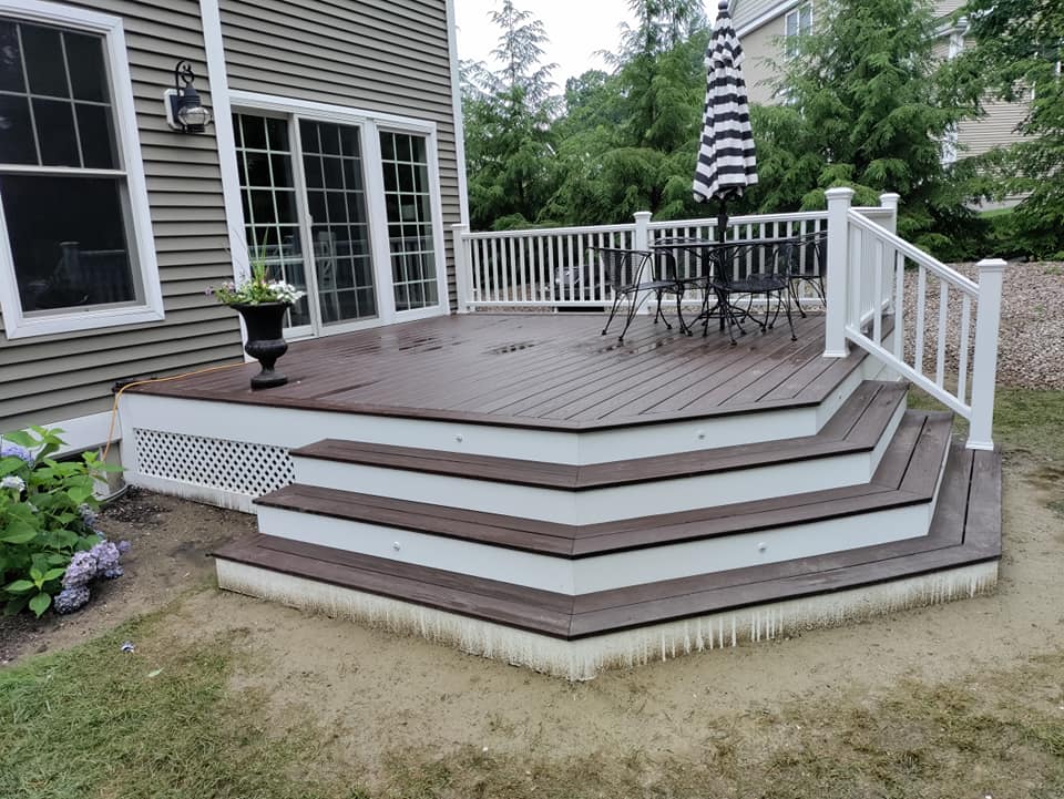 A deck with stairs and a table and chairs on it in front of a house.