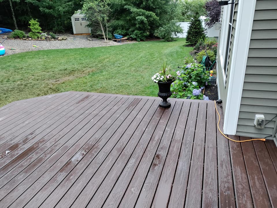 A wooden deck with a vase of flowers on it and a house in the background.