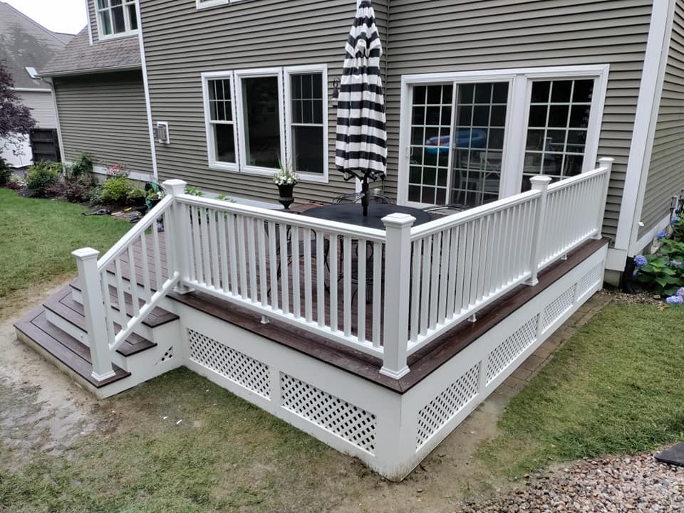 A white deck with a black and white striped umbrella is in front of a house.