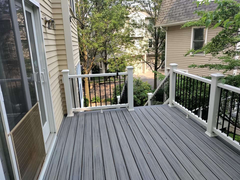 A gray deck with a white railing is next to a house.